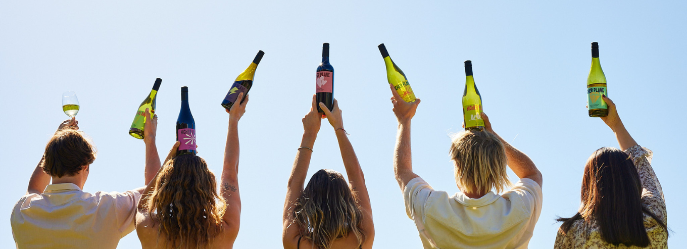 A group of people holding up Higher Plane wine bottles 